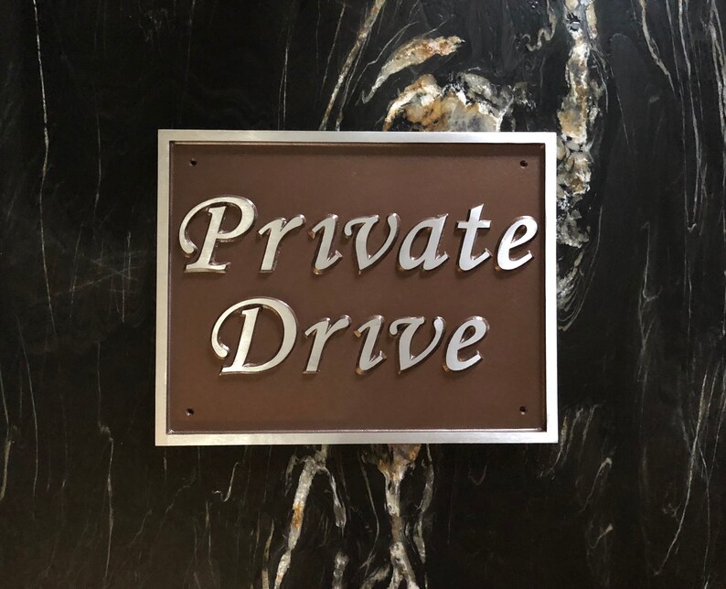 以下が含まれることがあります： 「Private Drive」と銀色の文字で書かれた、銀色の縁取りのある茶色の金属製の標識です。