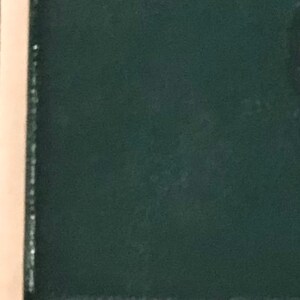 May include: A dark green fabric with a subtle texture. The fabric is framed by a light brown border.