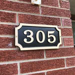 May include: A gold-coloured house number plaque with a black background and white numbers. The plaque reads "305".