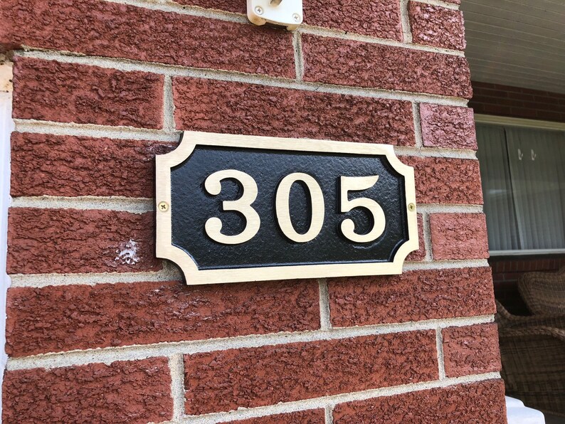 May include: A gold-coloured house number plaque with a black background and white numbers. The plaque reads "305".
