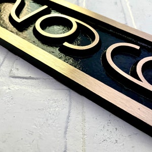 May include: A gold-colored metal sign with the word "CO" in raised lettering on a black background. The sign has a brushed gold border.