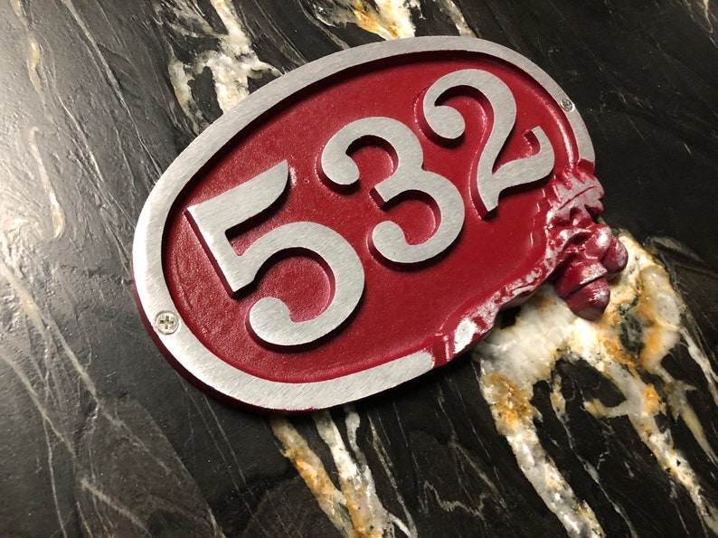 May include: A red oval-shaped house number sign with silver lettering. The number 532 is displayed on the sign. The sign is slightly damaged on the right side.