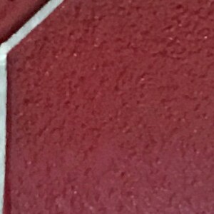May include: A close-up of a burgundy red surface with a white border. The surface has a textured, grainy appearance.