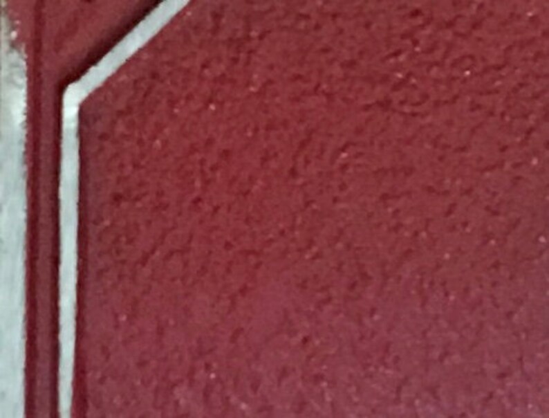 May include: A close-up of a burgundy red surface with a white border. The surface has a textured, grainy appearance.