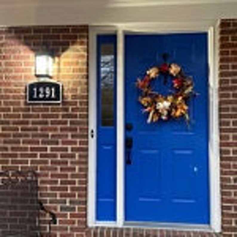 May include: A blue front door with a autumn-themed wreath and a house number "1391" on the brick wall.