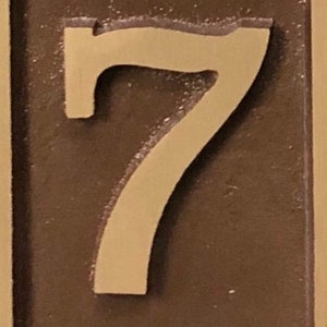 May include: A close-up of a brown plaque with a raised, cream-colored number "7" on it.