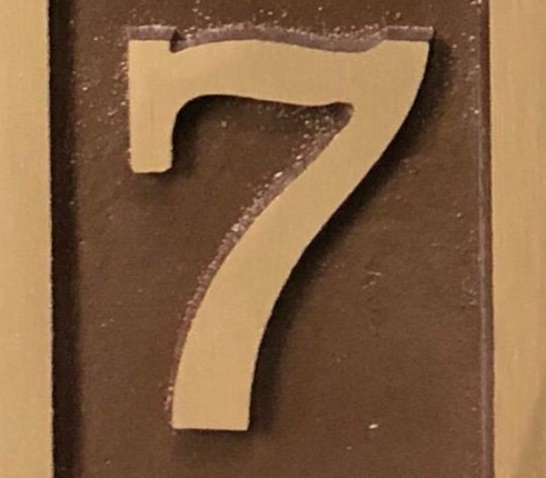 May include: A close-up of a brown plaque with a raised, cream-colored number "7" on it.