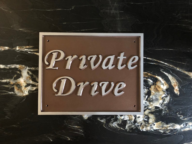 以下が含まれることがあります： 「Private Drive」と刻まれた、銀色の縁取りのある茶色の金属製の標識。