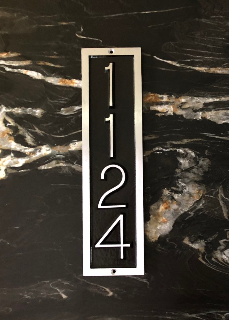 May include: A vertical silver metal house number plaque with a black background. The numbers 1124 are displayed in white.