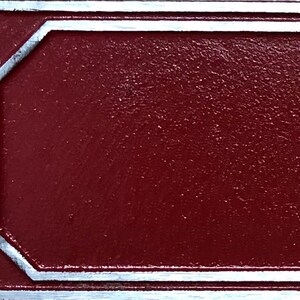 May include: A close-up of a red metal sign with a silver border. The sign has a textured surface.