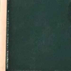 May include: A dark green fabric with a subtle texture. The fabric is framed by a light brown border.