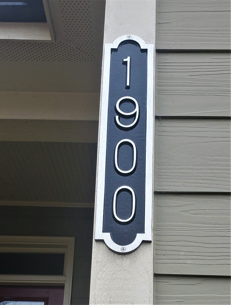 May include: A black and white house number sign with the number 1900 on it. The sign is mounted on a white post.