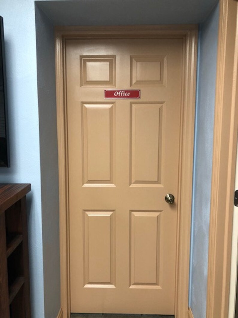 May include: A tan wooden door with a red sign that says "Office" on it. The door has six panels and a brass door knob.