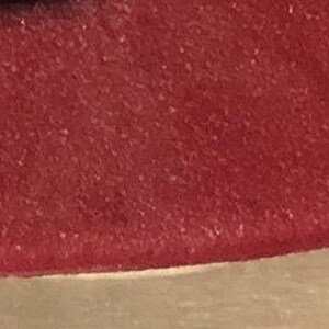 May include: Close-up of a deep red, textured surface. The surface has a slightly rough, grainy texture.