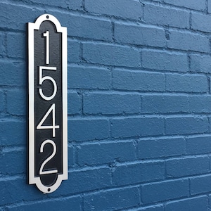 May include: A vertical silver and black house number sign with the number 1542 on a blue brick wall.