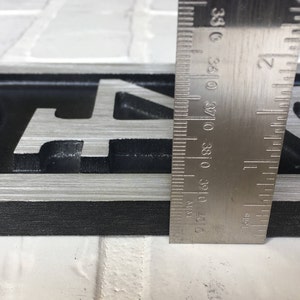 May include: Close-up of a silver metal house number plaque with the numbers "943" in black. The plaque is 1 inch wide and is measured with a ruler.