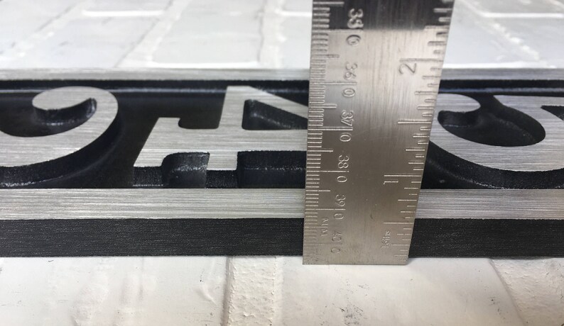May include: Close-up of a silver metal house number plaque with the numbers "943" in black. The plaque is 1 inch wide and is measured with a ruler.
