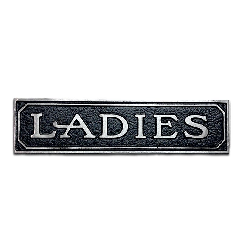 May include: A black and silver metal sign with the word "LADIES" in white lettering.