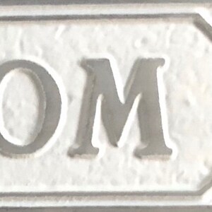 May include: White ceramic sign with the word "OM" in raised black lettering.
