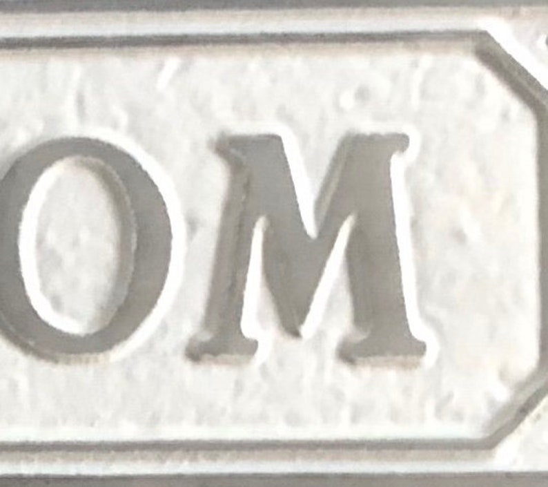 May include: White ceramic sign with the word "OM" in raised black lettering.