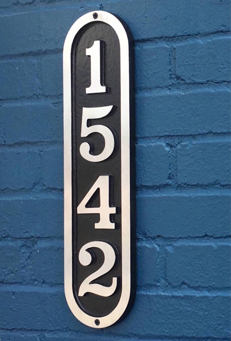 K&ouml;nnte beinhalten: Ein vertikales, ovales Hausnummernschild mit schwarzem Hintergrund und silbernen Zahlen. Die Zahlen sind 1542.