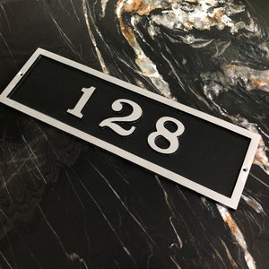 May include: A silver rectangular house number plaque with a black background. The number 128 is printed in silver on the plaque.