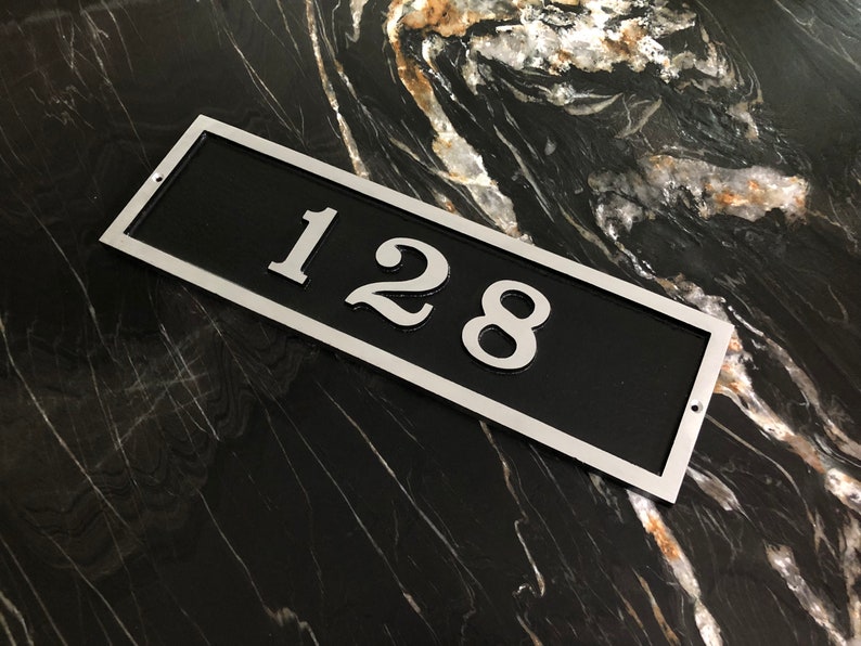 May include: A silver rectangular house number plaque with a black background. The number 128 is printed in silver on the plaque.