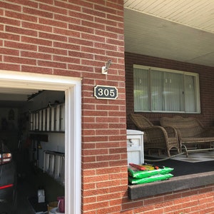May include: A brick house with a garage door and a porch. The house number 305 is displayed on the front of the house. There are two wicker chairs and a wicker sofa on the porch.