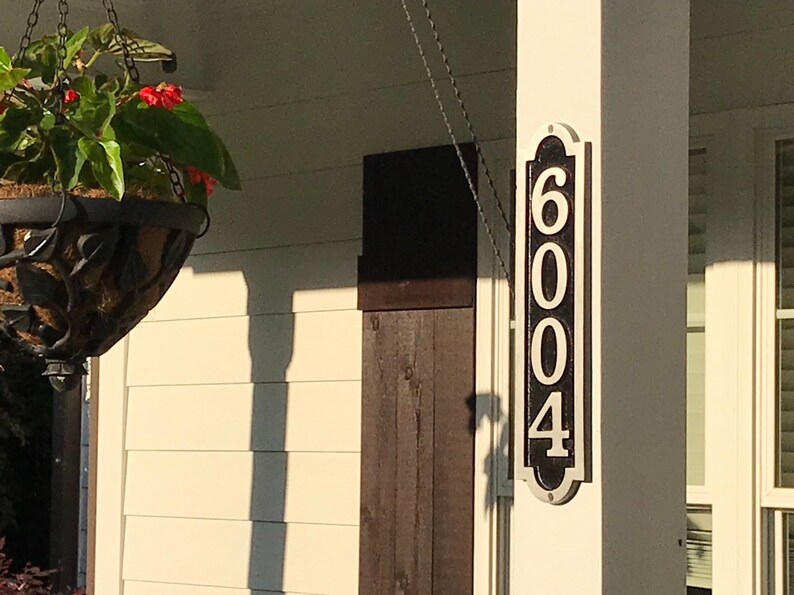 May include: A black and white house number sign with the number 6004 on it. The sign is mounted on a white column.