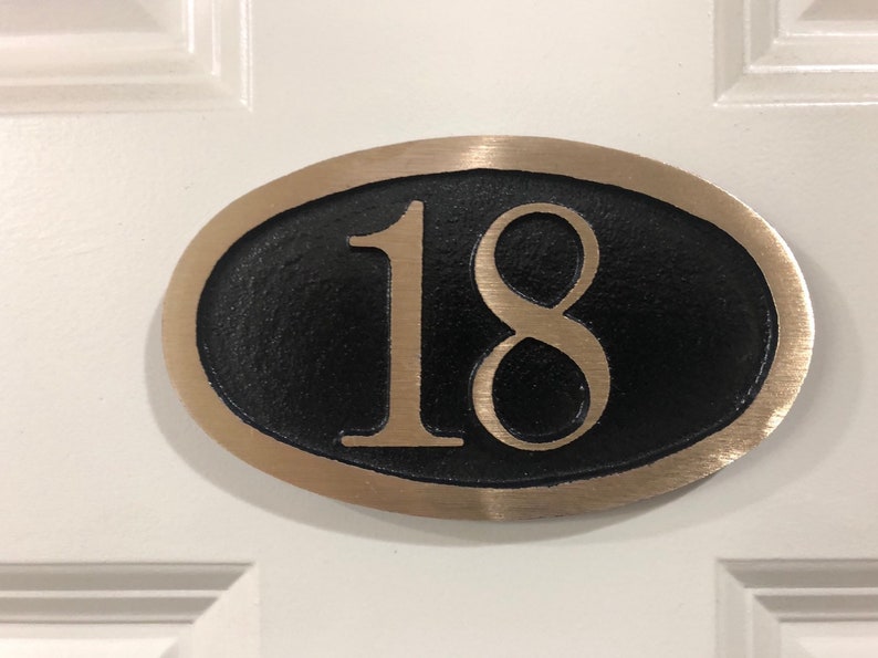 May include: A brass oval-shaped house number plaque with a black background and the number 18 in gold lettering.