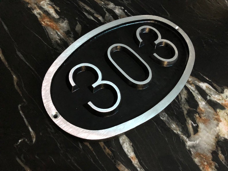 May include: A silver oval-shaped sign with a black background and the number 308 in raised silver lettering.