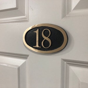 May include: A gold oval-shaped door number plaque with the number 18 in black lettering.