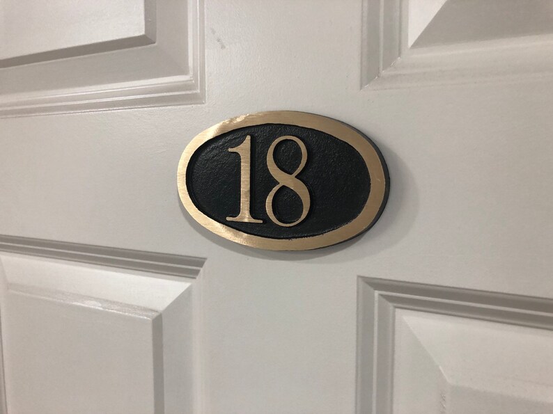 May include: A gold oval-shaped door number plaque with the number 18 in black lettering.