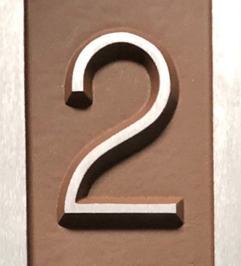 May include: A close-up of a silver number "2" embossed on a brown background.