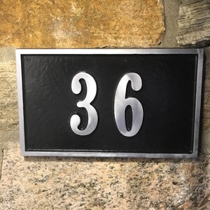 May include: A silver metal house number plaque with a black background. The number 36 is displayed in a silver font.