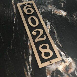 May include: A vertical house number plaque with a black background and gold trim. The numbers 6028 are displayed in white.
