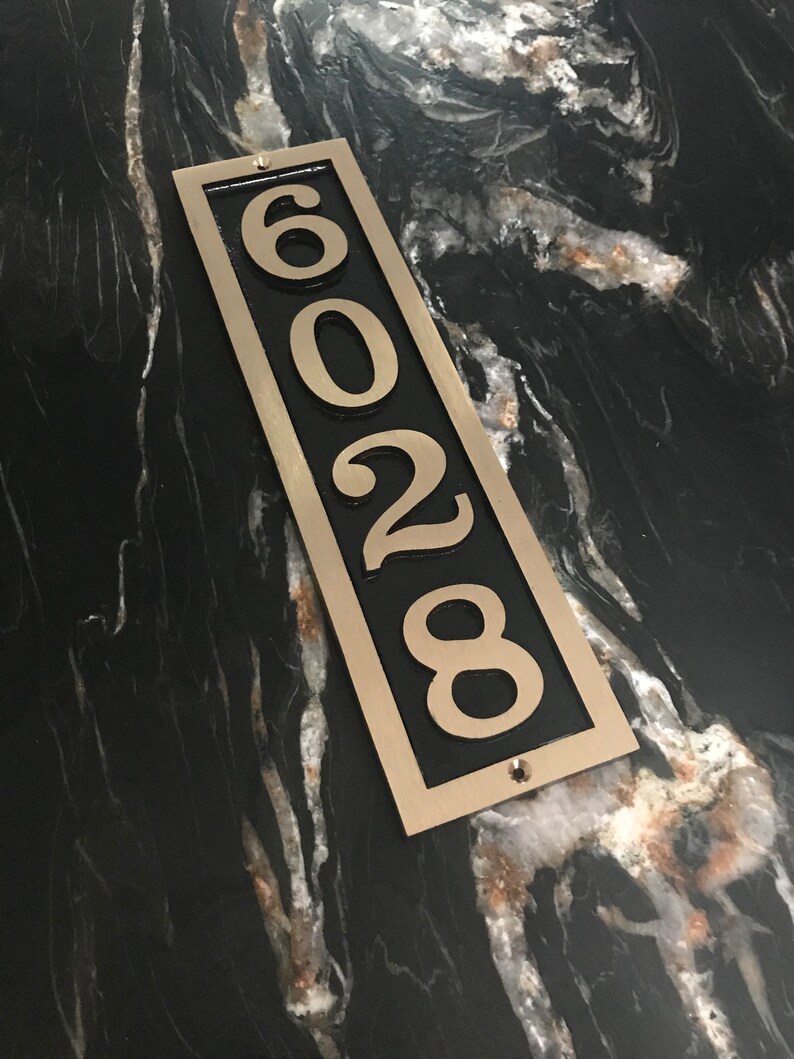 May include: A vertical house number plaque with a black background and gold trim. The numbers 6028 are displayed in white.