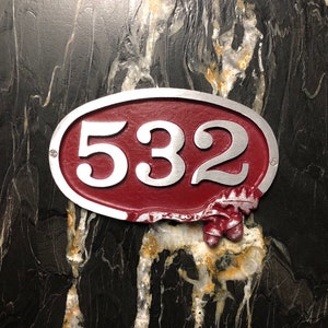 May include: A red oval-shaped house number sign with silver lettering. The number 532 is displayed on the sign.