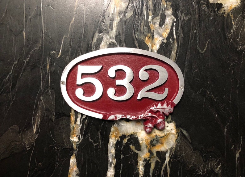 May include: A red oval-shaped house number sign with silver lettering. The number 532 is displayed on the sign.
