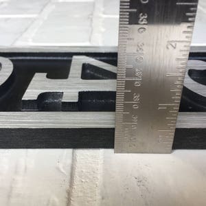 May include: A close-up of a black and silver house number sign with the numbers "94" and a decorative swirl. The sign is being measured with a ruler.