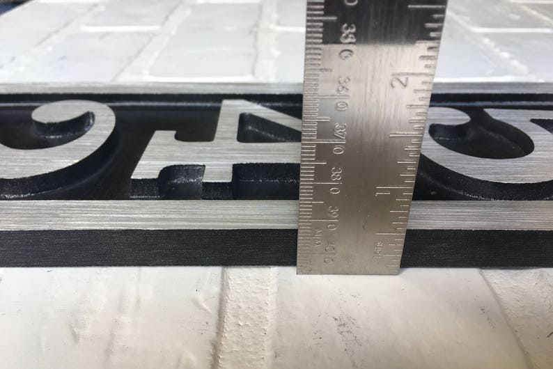 May include: A close-up of a black and silver house number sign with the numbers "94" and a decorative swirl. The sign is being measured with a ruler.