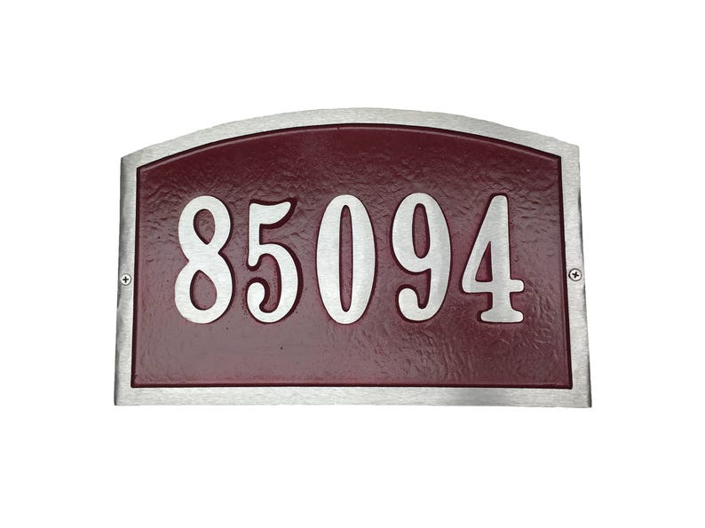 May include: A silver-framed house number plaque with a burgundy background. The number 85094 is displayed in a silver, stylized font.