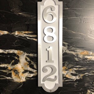 May include: A silver metal house number plaque with white numbers. The numbers are 6812.