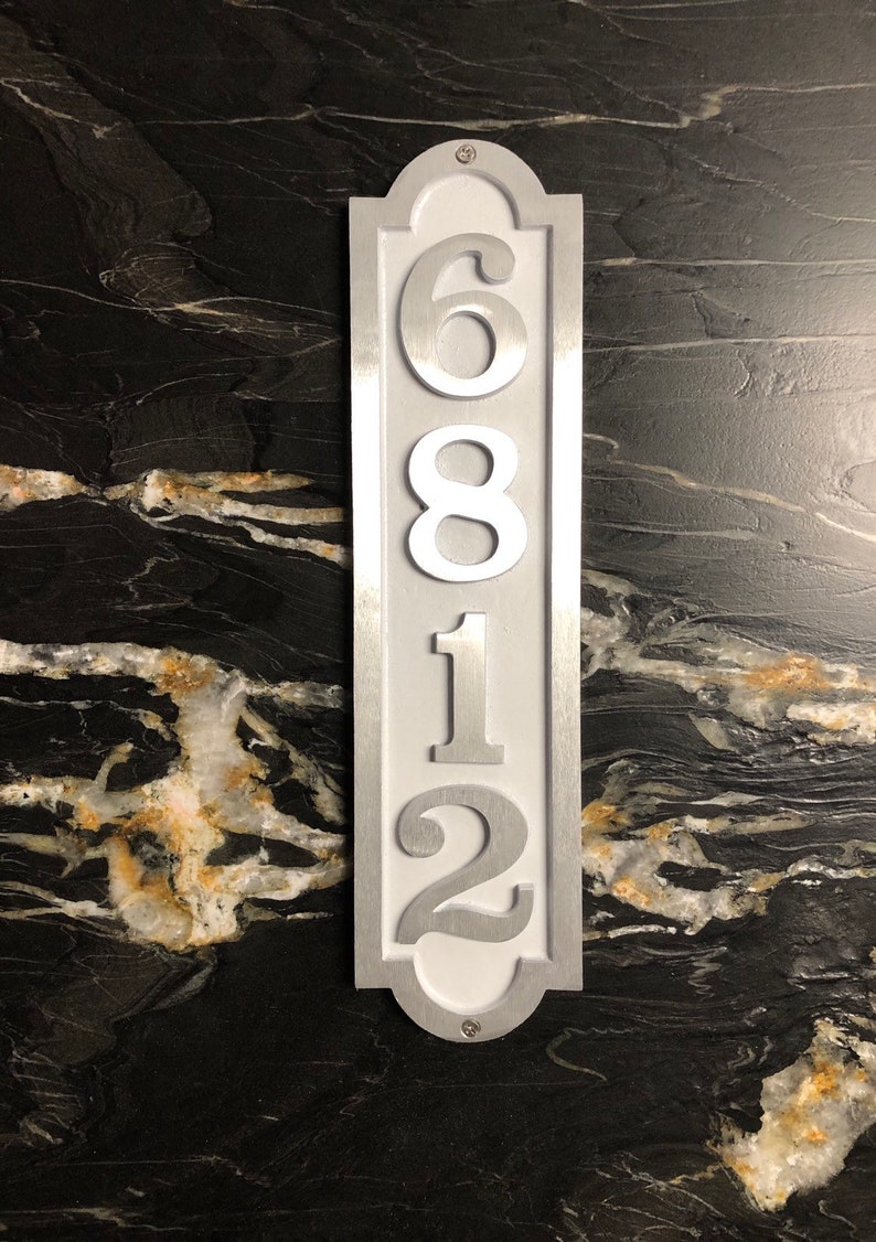 May include: A silver metal house number plaque with white numbers. The numbers are 6812.