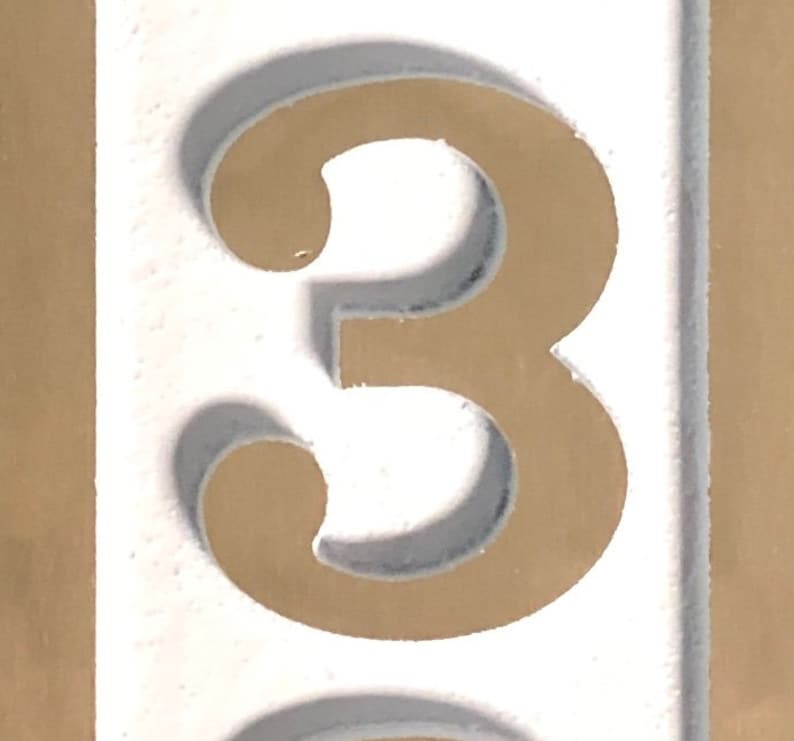 May include: A white number three with a brown outline. The number is on a white background.