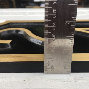 May include: A black metal house number sign with gold trim. The number "2" is visible. The sign is 3 7/8 inches tall.