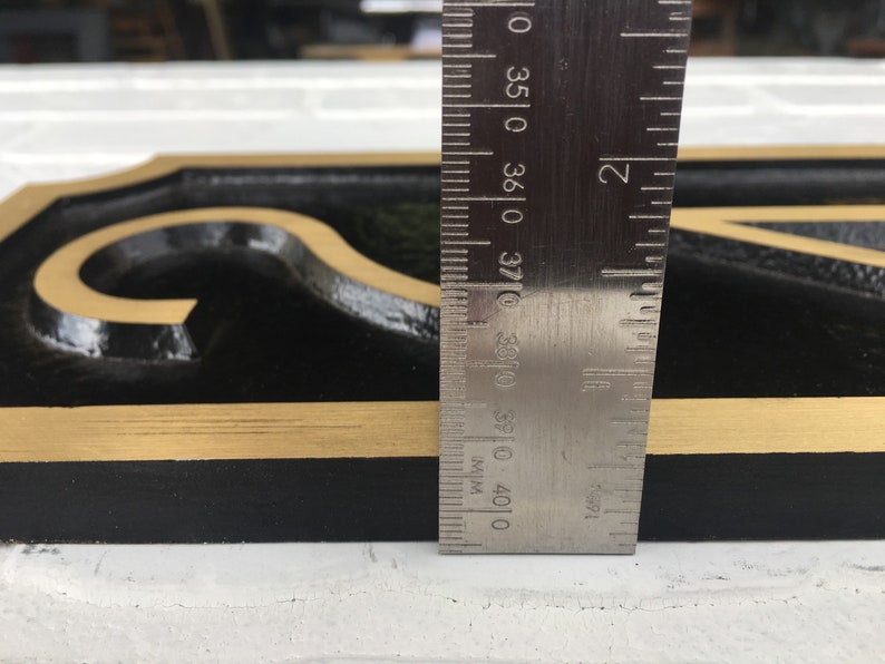 May include: A black metal house number sign with gold trim. The number "2" is visible. The sign is 3 7/8 inches tall.