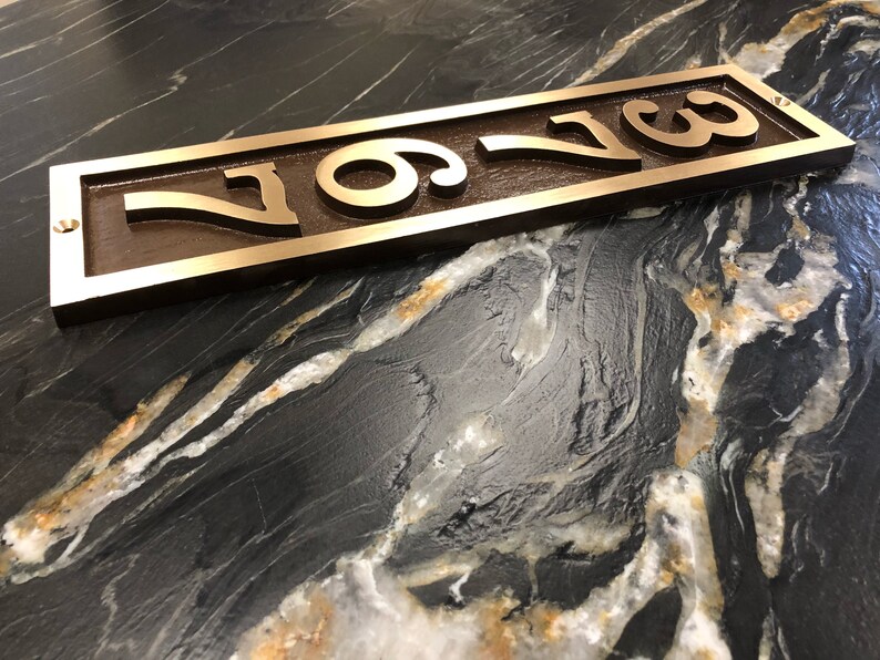 May include: A bronze house number plaque with the number "709" engraved in a raised, stylised font. The plaque is rectangular and has a slightly weathered finish.