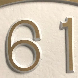 May include: A close-up of a white surface with the numbers 61 in gold raised lettering.