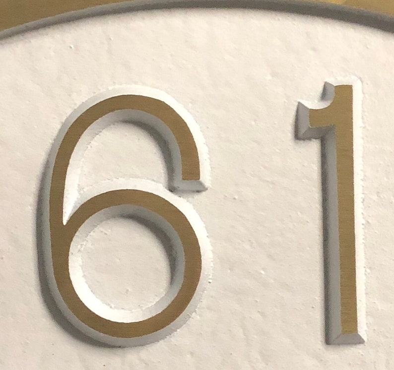 May include: A close-up of a white surface with the numbers 61 in gold raised lettering.